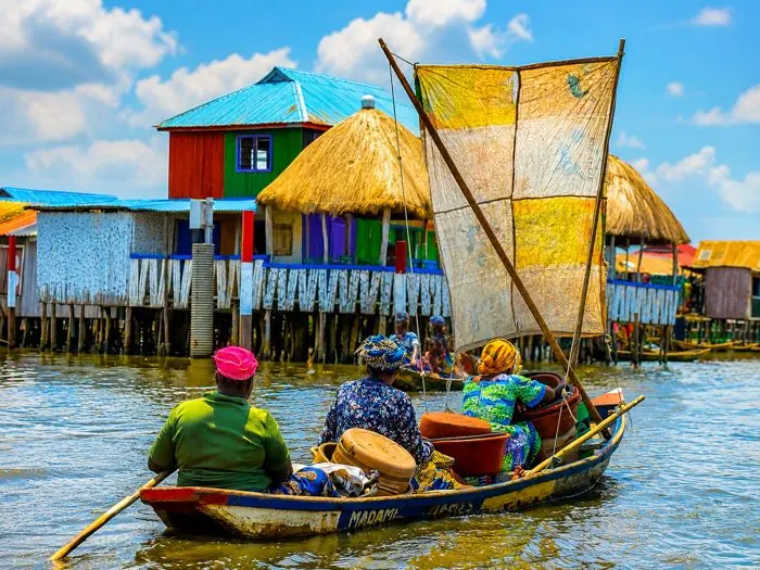 Femmes en pirogue à voile devant des maisons colorées sur pilotis à Ganvié.