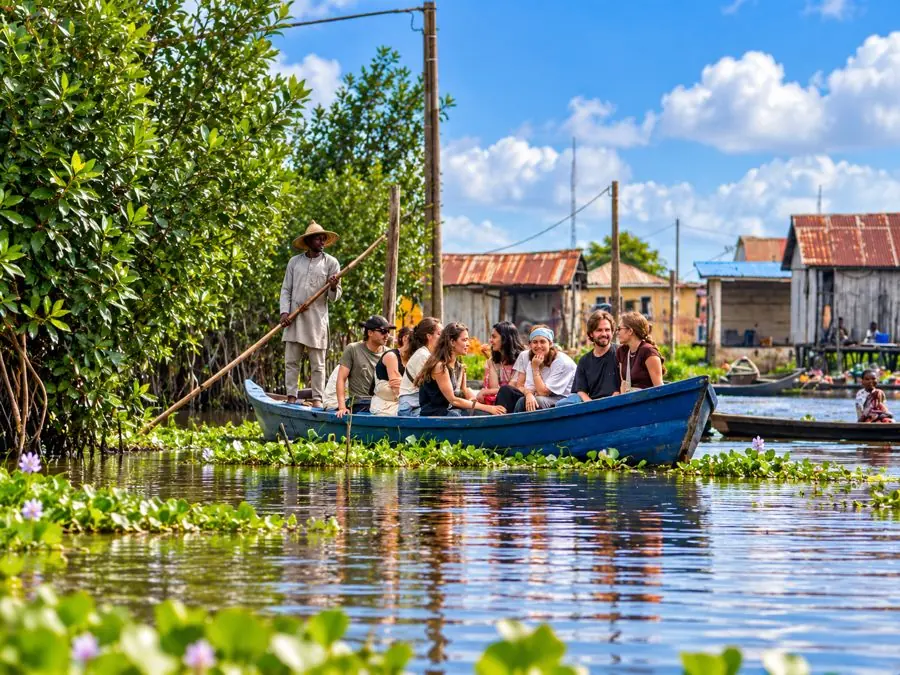 Groupe de visiteurs en pirogue avec un piroguier lors d’une visite guidée de Ganvié, entre jacinthes d’eau et maisons du village.
