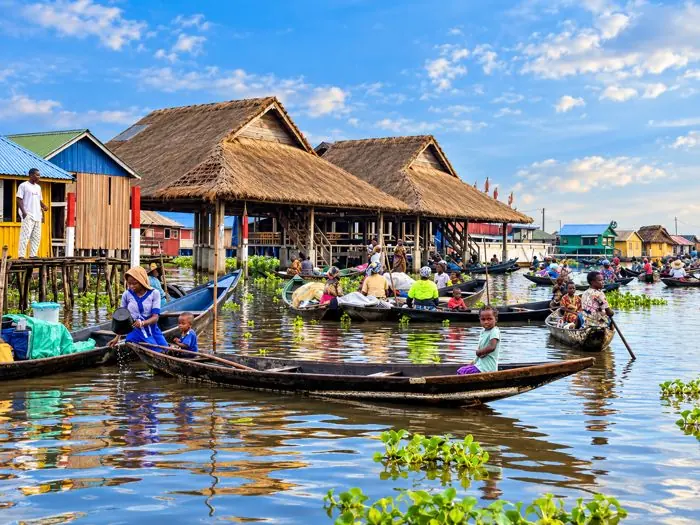 Pirogues chargées et maisons sur pilotis aux toits de chaume, scène de marché sur l’eau à Ganvié.