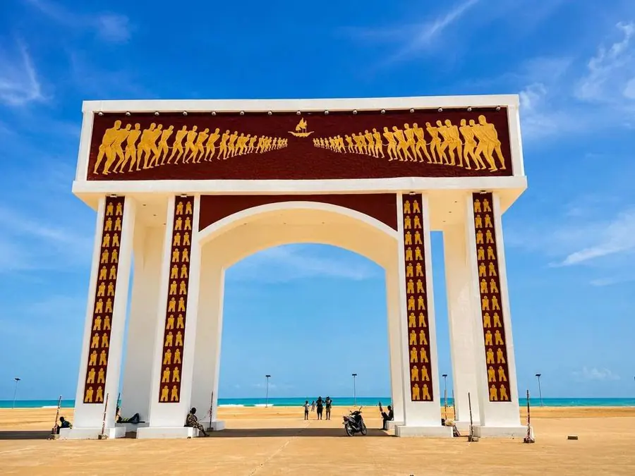 Porte du Non-Retour à Ouidah au Bénin, sous un ciel bleu, face à l’océan Atlantique.