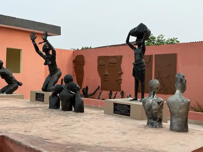 Sculptures commémoratives de l’esclavage devant un mur orné de bas-reliefs à Ouidah.