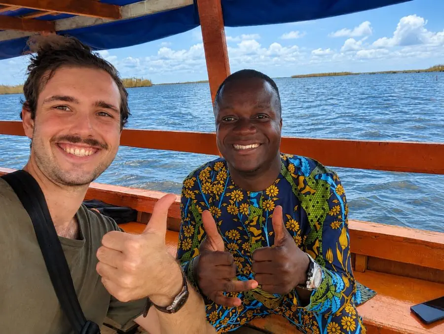 Théophile, guide local de Visit Ganvié Tourism, avec un visiteur, pouces levés, dans une pirogue sur le lac Nokoué.