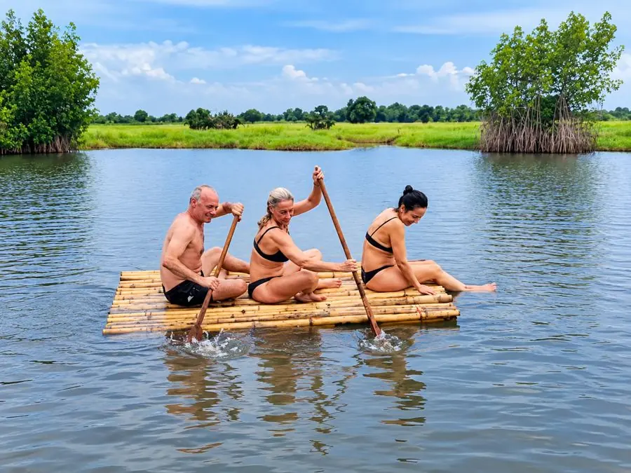 Trois visiteurs pagaient sur un radeau en bambou devant la mangrove à Gogotinkpon au Bénin.