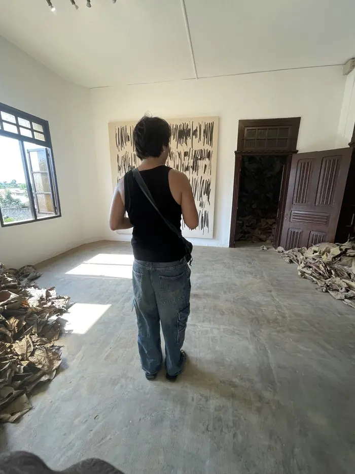 Visiteur de dos devant une grande toile dans une salle d’exposition d’art à Ouidah.