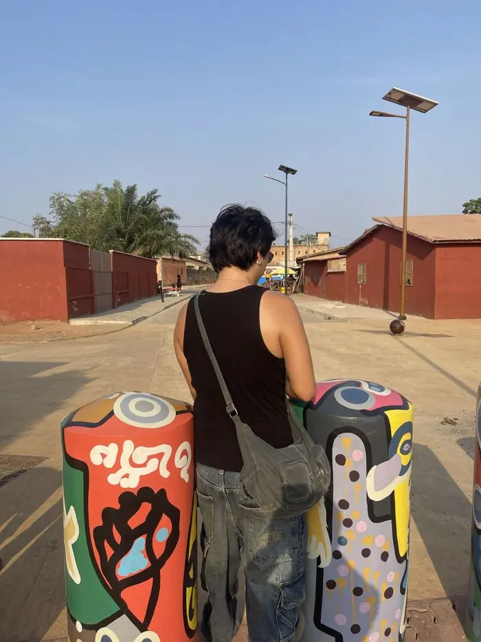 Visiteur de dos entre des bornes peintes de motifs colorés dans une rue de Ouidah.