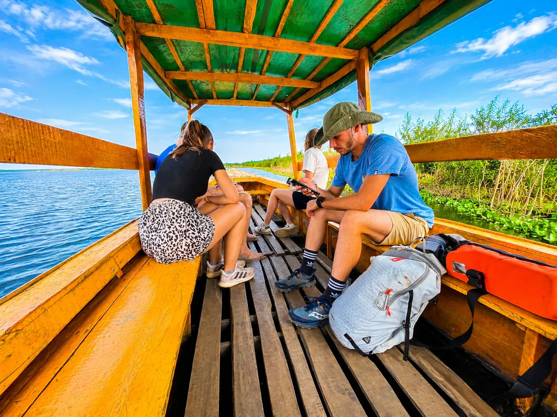 Visiteurs assis dans une pirogue couverte au toit vert, naviguant sur le lac le long de la végétation