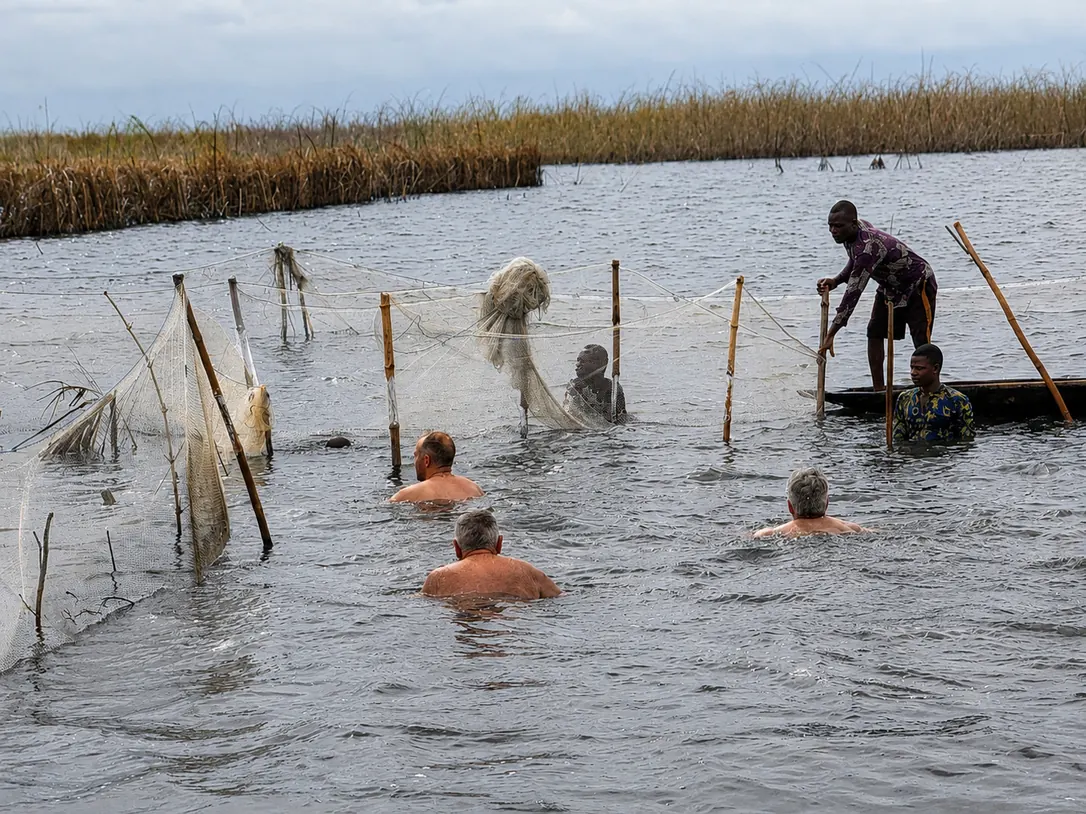 Visiteurs dans l’eau aux côtés de pêcheurs près de filets de pêche tendus sur des piquets