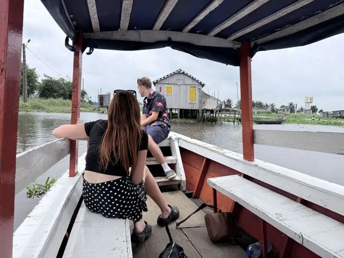 Visiteurs en pirogue couverte approchant d’une maison sur pilotis à Ganvié.