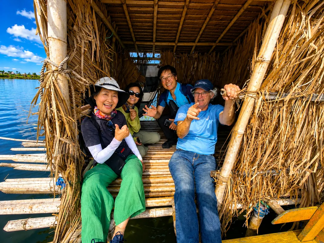 Quatre visiteurs souriants assis dans une cabane en bambou et en paille au-dessus de l’eau