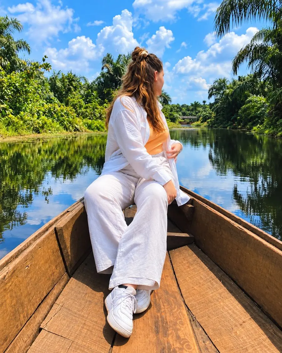 Visiteuse assise à l’avant d’une pirogue en bois sur la Rivière Noire d’Adjarra, bordée de palmiers, au Bénin.